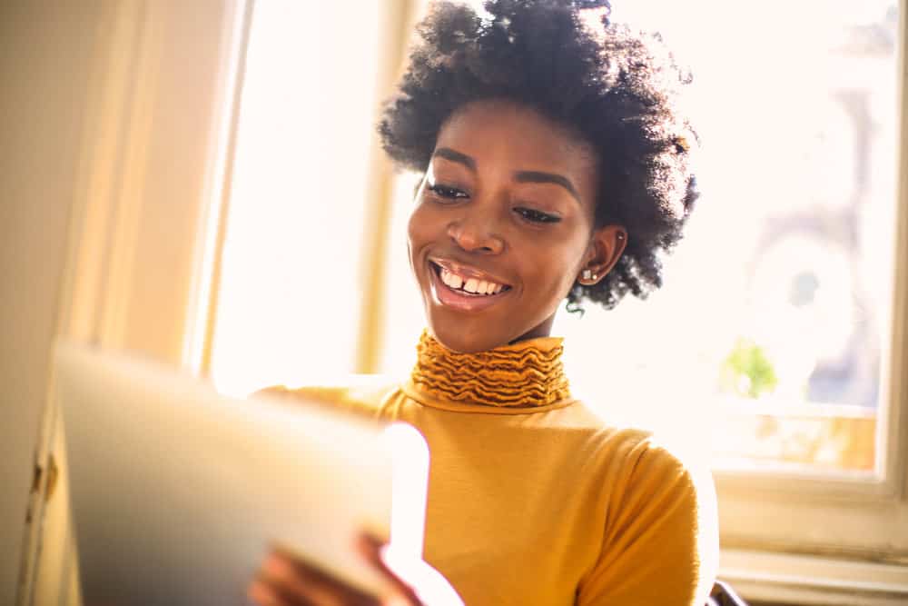 Dark-skinned black girl wearing an orange shirt trying a new hair style app before going to the hairdresser.