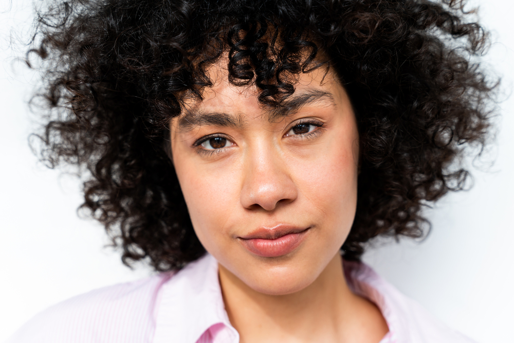 A beautiful Latino young woman with thin hair that's using Coconut milk shampoo and argan oil in her hair regimen.