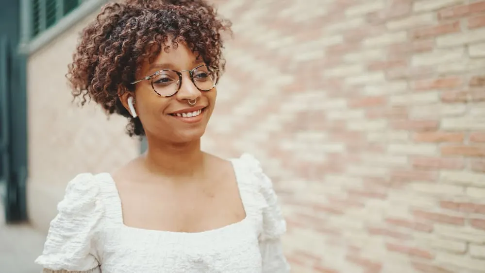 Young woman with really curly hair walking outdoors while listening to a podcast about hair loss using AirPods.