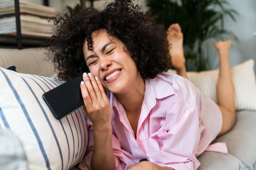 A Latino woman with curly fine hair talking to a friend at home about the best OGX shampoos for colored hair.