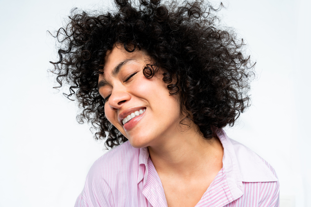 A happy female wearing naturally curly hair styled with coconut oil, egg white proteins, and tea tree oil.
