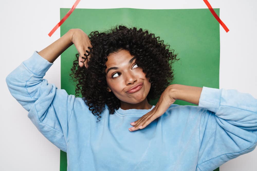 An amusing black woman with shoulder-length hair growth has her natural curls styled with tea tree oil.