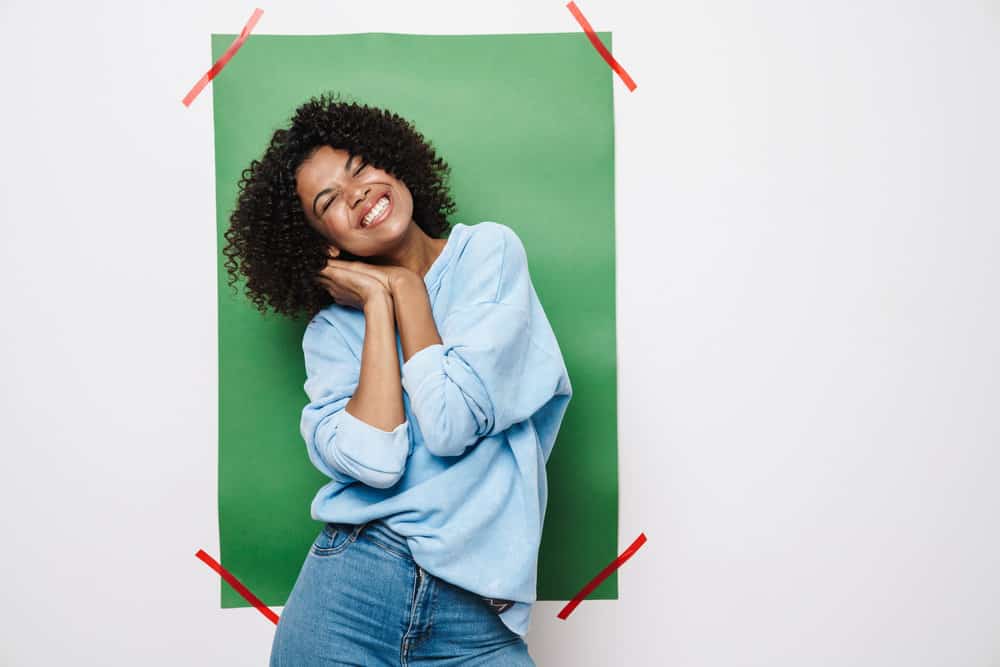 A cheerful black woman with an irritated scalp and hair loss with curly thick hair having trouble with her scalp health.