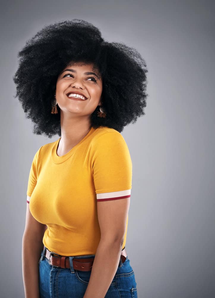 A black woman with natural curls in a wash-and-go hairstyle is seen wearing a gold-colored t-shirt.