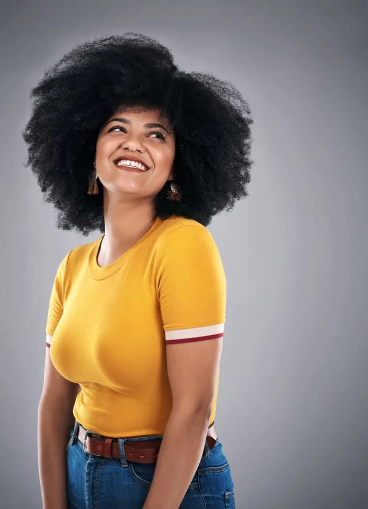 Why Is My Black Hair Turning Gold? 4 Causes & 3 Quick Fixes 8 A black woman with natural curls in a wash-and-go hairstyle is seen wearing a gold-colored t-shirt.