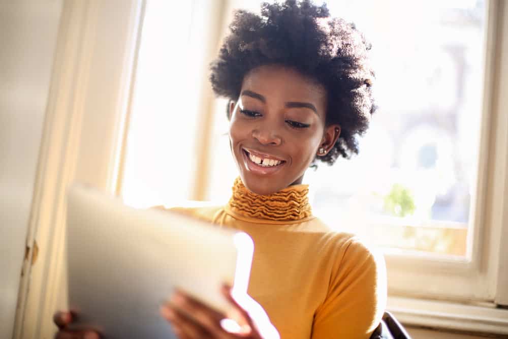 A young woman of African descent is shown using a hairstyle-finding software on her iPad.