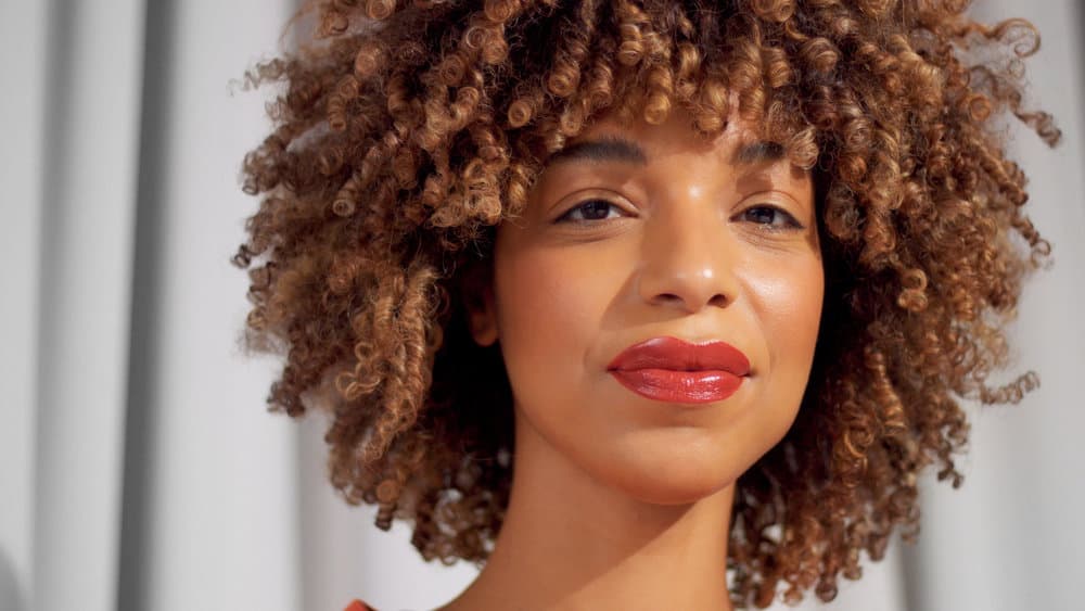 Mixed race black woman with a thick hair texture has Shirley Temple curls on blonde, brown, and gray hair strands.