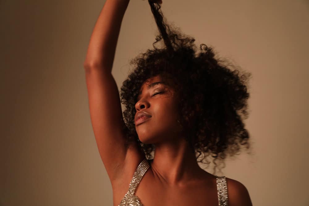 Cute African American female measuring her hair's length after using personalized shampoo in her hair regimen.