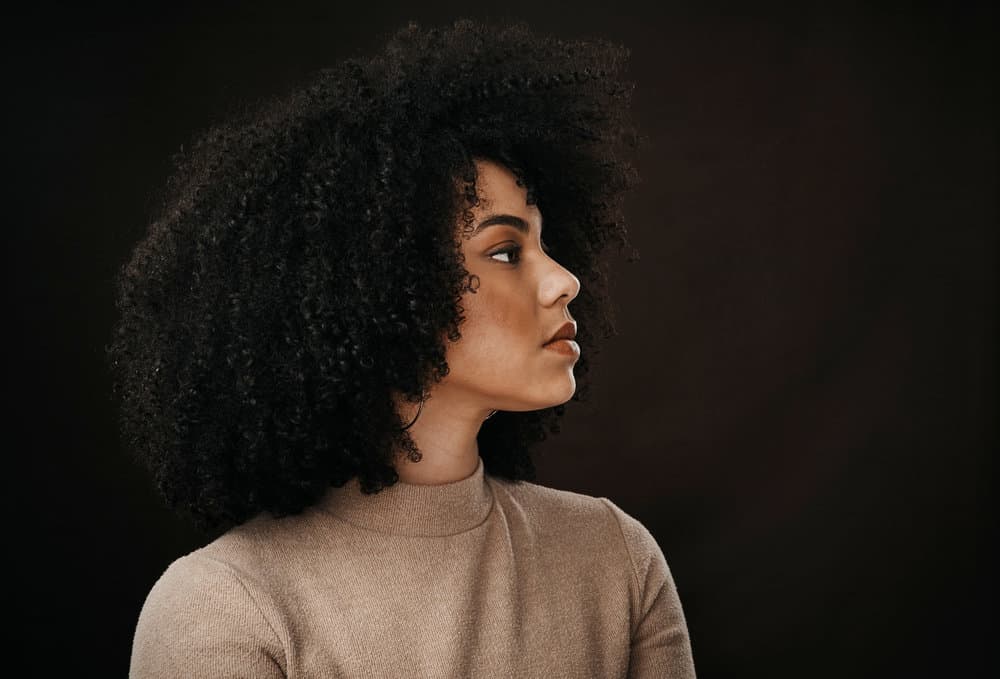 Thoughtful young lady with bouncy curls styled with a clean hairbrush after a regular cleaning process.