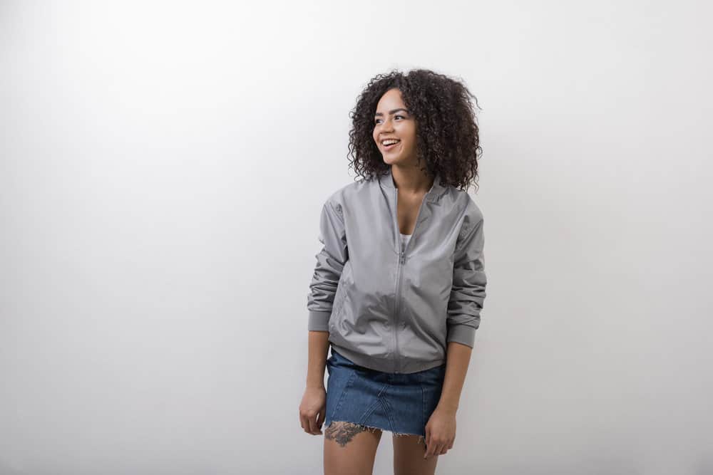 A black lady wearing a gray jacket and a blue jean skirt that's just starting her natural hair journey.