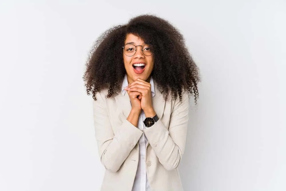 Cute young black girl with wavy hair after drying her wet hair wearing it shoulder length with a beige business suit.