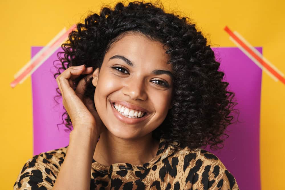 A cheerful black female with brown hair and a flaky scalp that's treating dandruff with a sulfate-free shampoo.