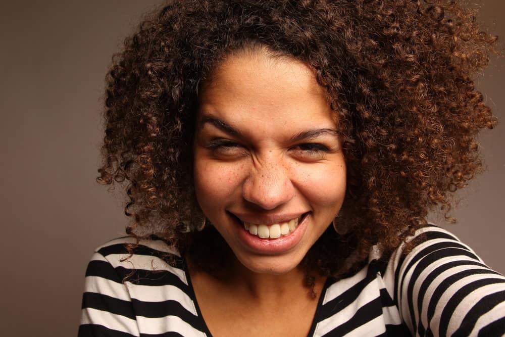 Light-skinned black woman with medium brown natural curls who is wearing semi-permanent hair color on her head.