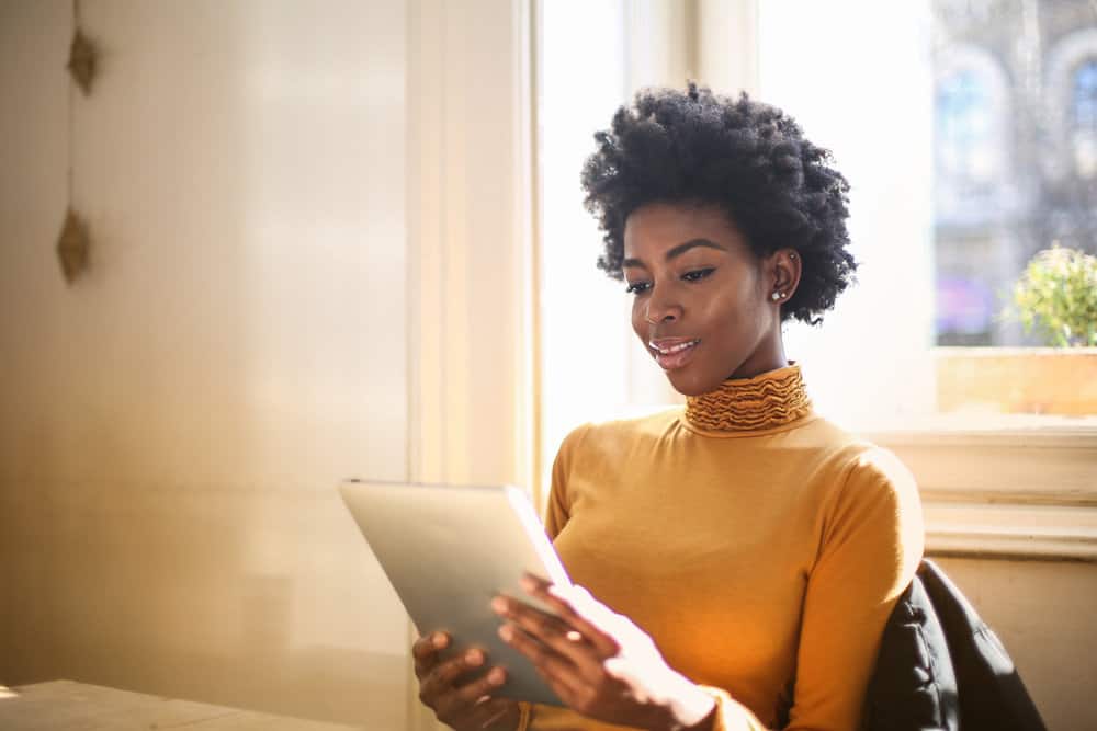 A cute black girl with long hair is using an app for bad hair days on her iPad to choose the best style for the day.