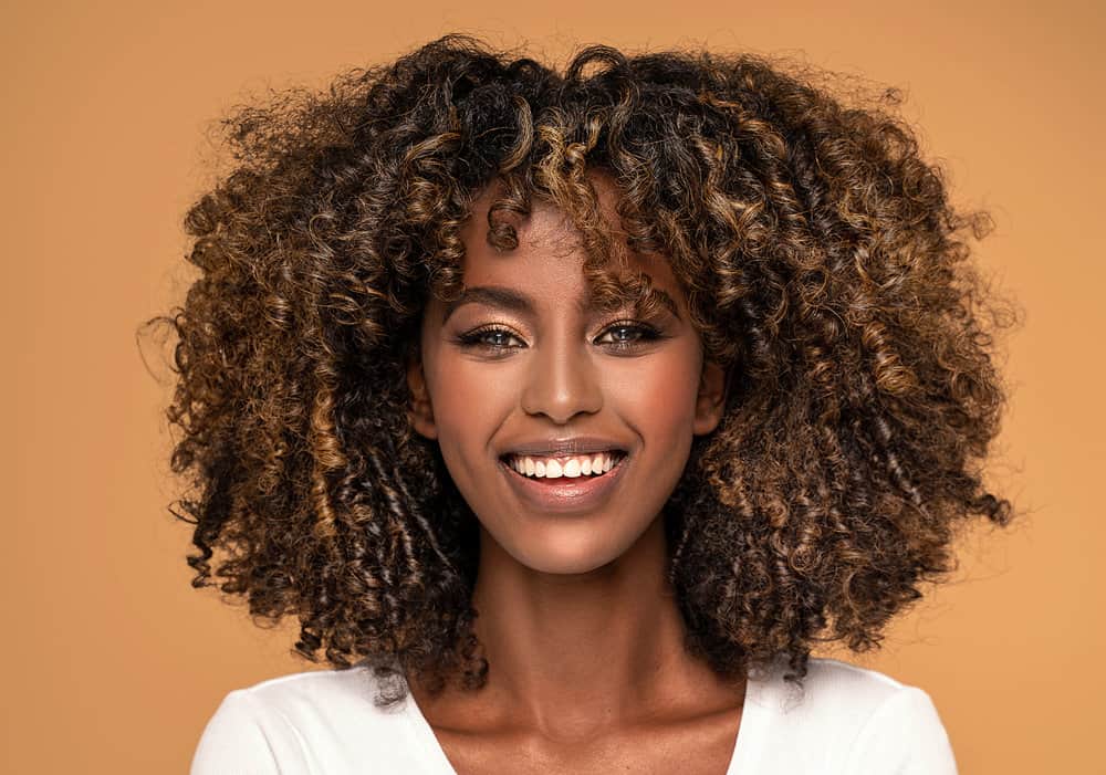 Young African lady with an oval face shape and kinky hair embracing the classic fringe bottleneck bang trend.