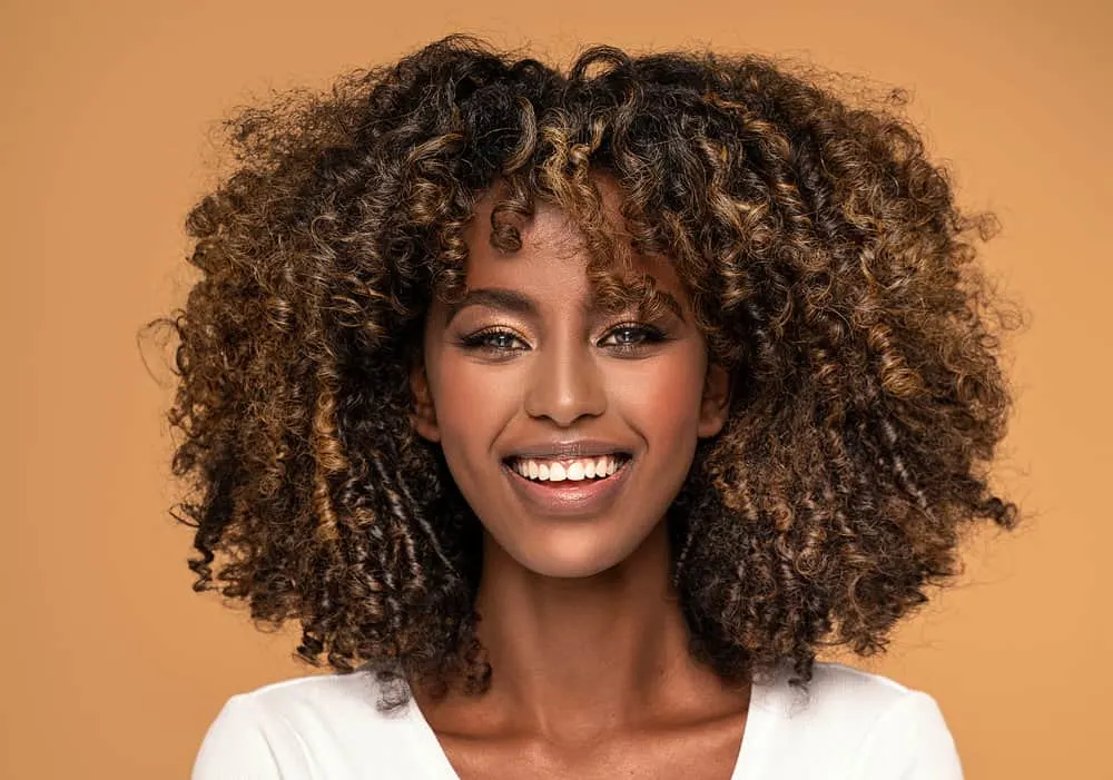 What Are Bottleneck Bangs? How to Cut and Style DIY Bangs 1 Young African lady with an oval face shape and kinky hair embracing the classic fringe bottleneck bang trend.