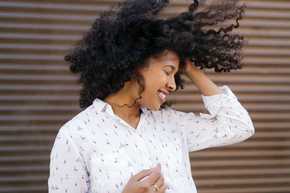 Beautiful black woman with type 3a naturally curly hair blowing in the wind wearing a white dress shirt.