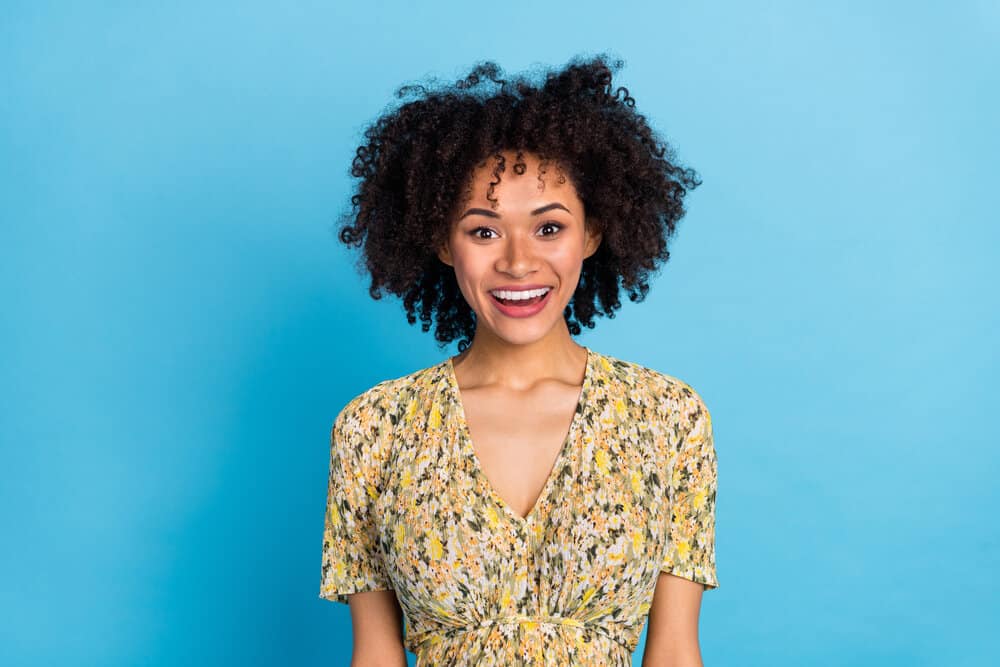 Cute young African American female with fine hair follicles wearing a curly hairdo styled with coconut oil and hot tools.