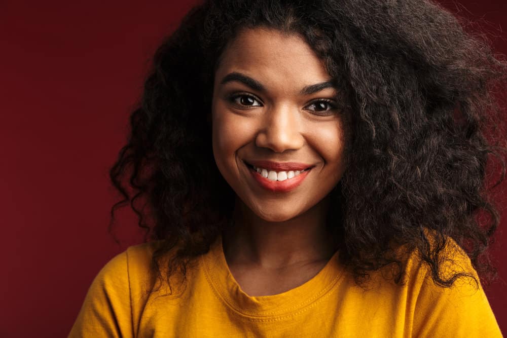 Cute young African American female with bone dry wavy hair follicles styled with a blow dryer and coconut oil.