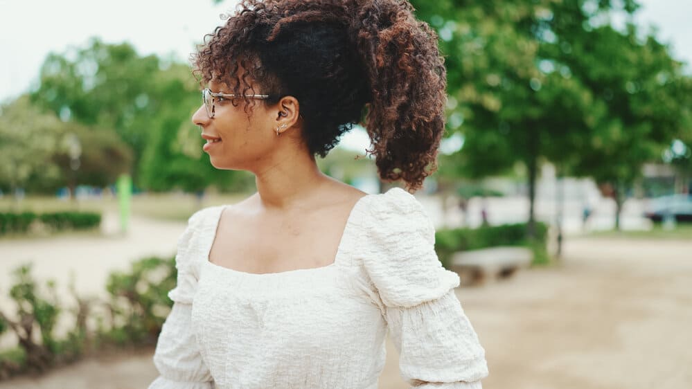 A smiling young woman with curls that were pin-straight as a kid now has a wavy curly hair pattern.