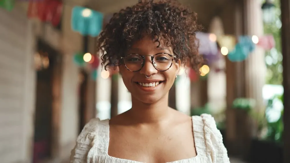 A light-skinned black girl with naturally curly hair follicles wearing her beautiful curly hair in a pineapple updo.