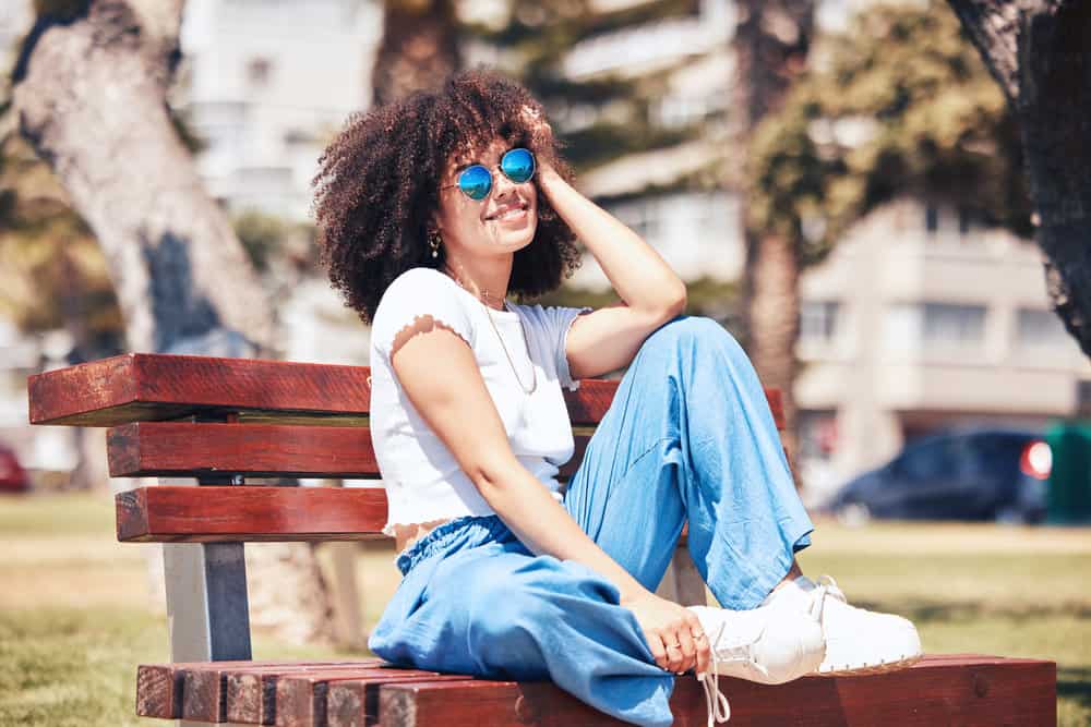 A cheerful female with a naturally curly hair type styled with olive oil and Shea Moisture leave-in styling gel.