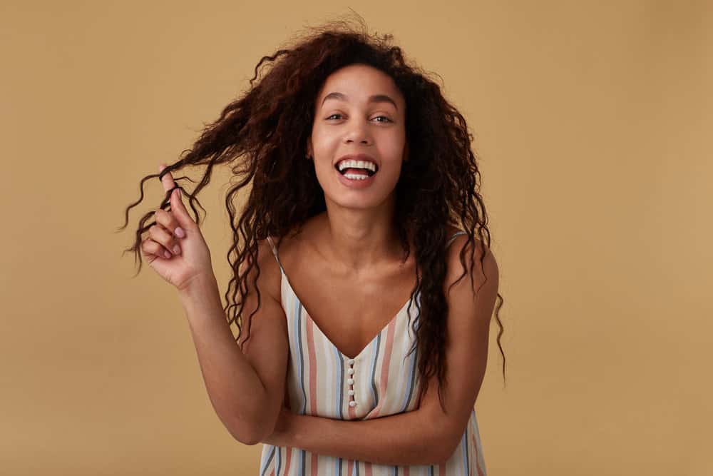 Joyful black female with thick hair and heat-free curls wearing her hair in bouncy waves after using low-heat tools.