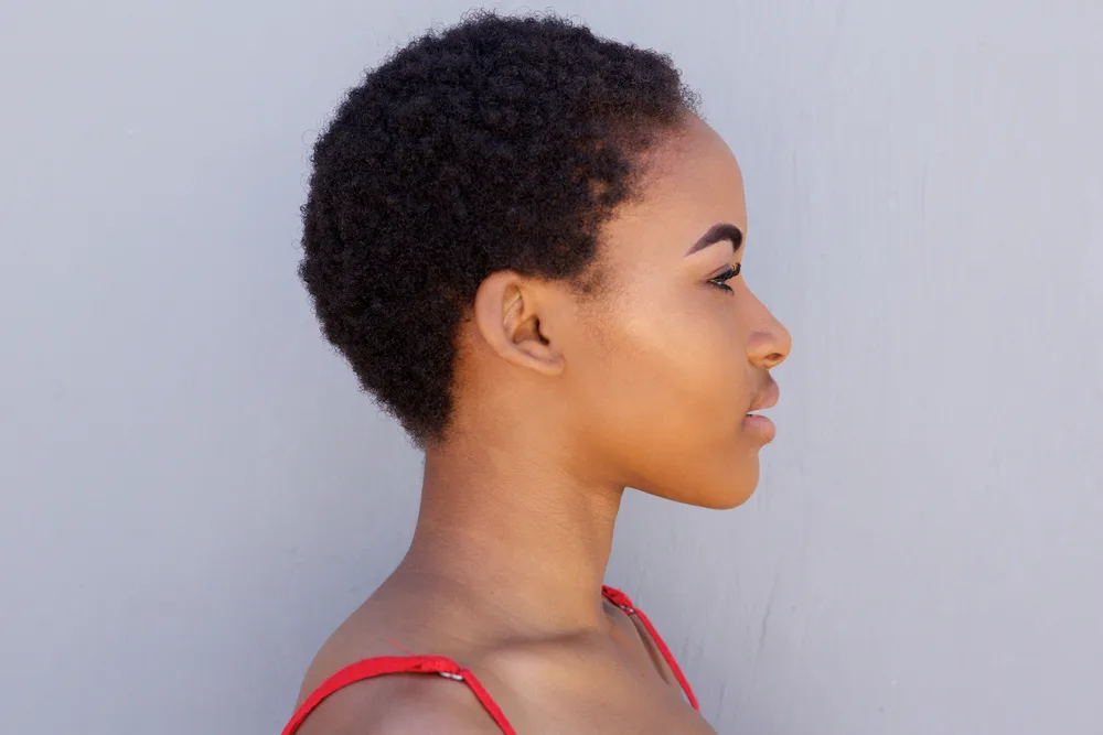 A young black lady after big chopping wearing her kinky, coily hair strands in a traditional wash-and-go hairstyle.