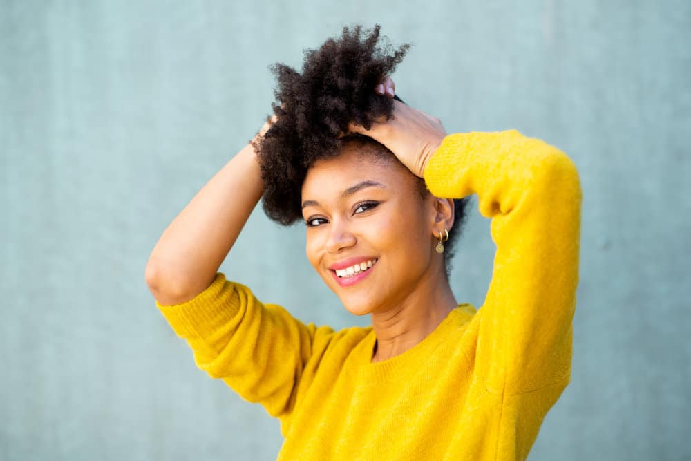 A young black woman putting her hair up in a protective hairstyle.