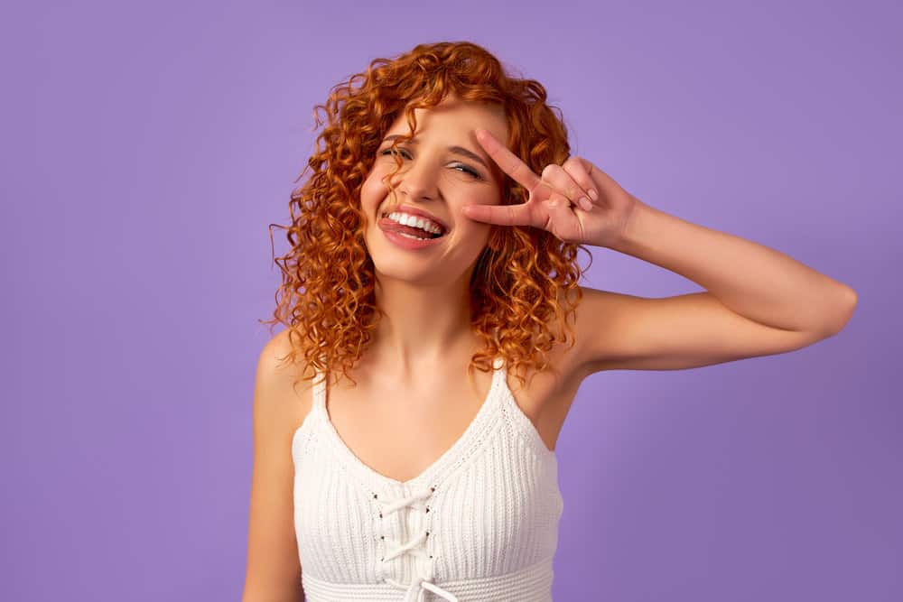 A young female with a light brown shade of wavy hair is making a funny face while wearing a white shirt.