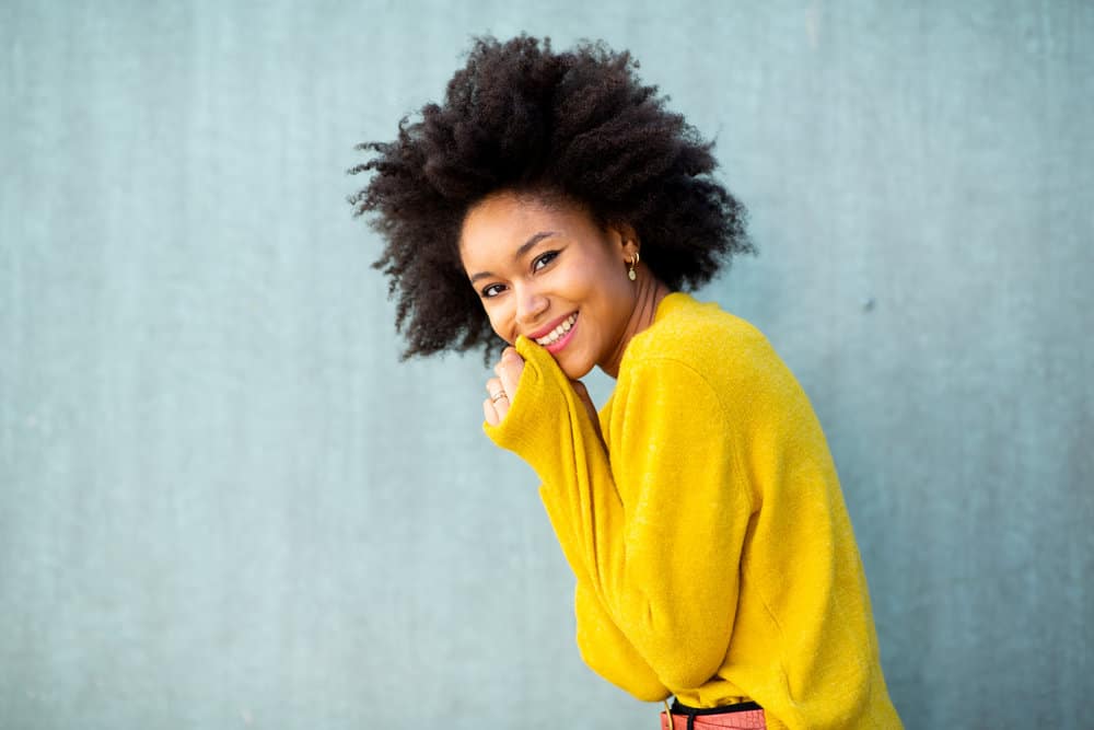A smiling young African American female with dry hair in an afro hairdo styled with hair butter and curl refresher.