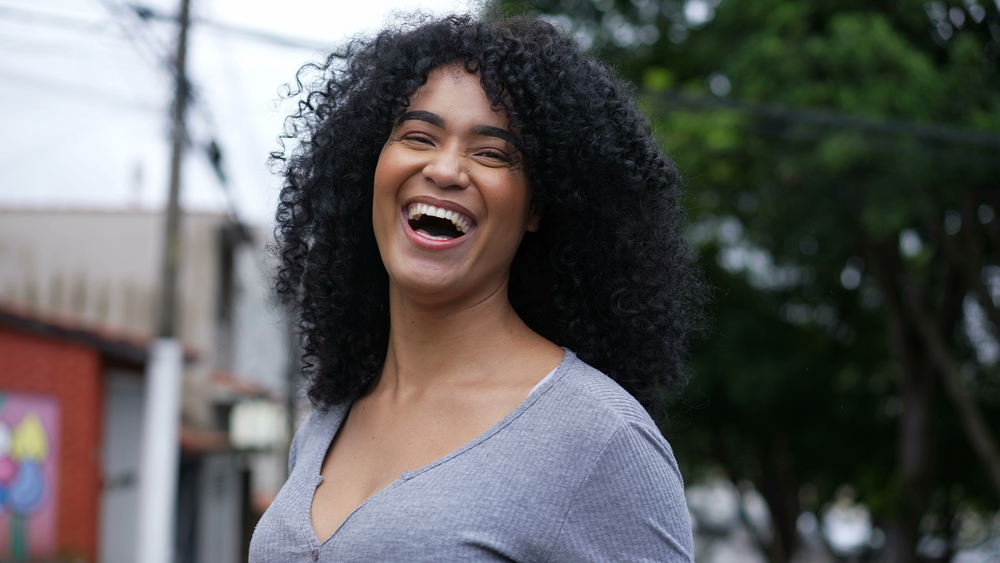 A Black lady with mild acne has 4A curls styled with a wide-tooth comb.