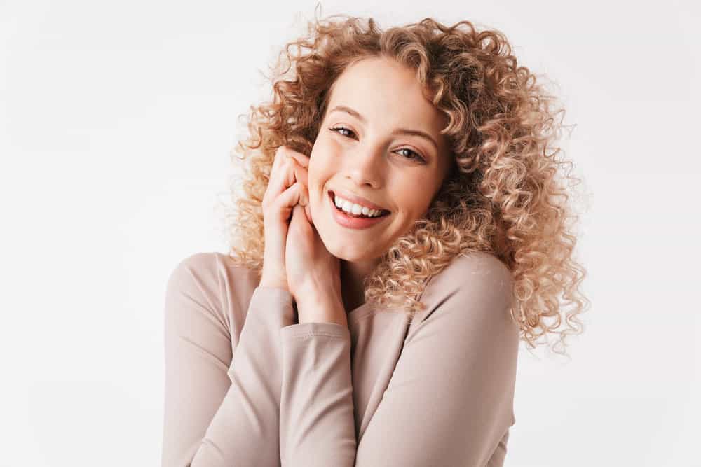 A cheerful young white girl with a dark brown natural hair color and a balayage hair-do on a medium hair length.