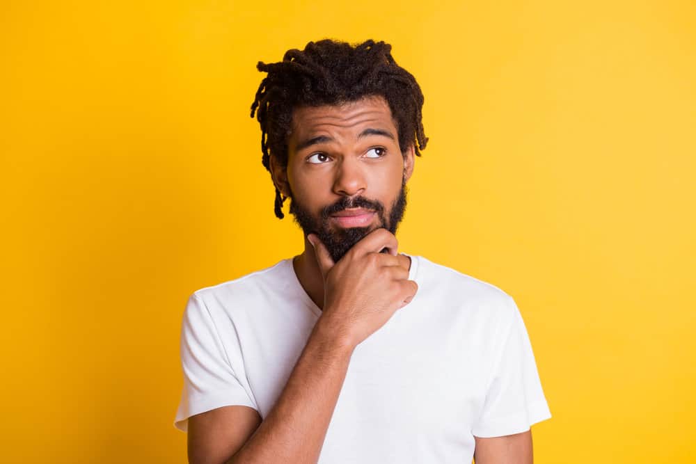 Dark skin man wondering long it will take his free-form dreads to reach middle-back length.