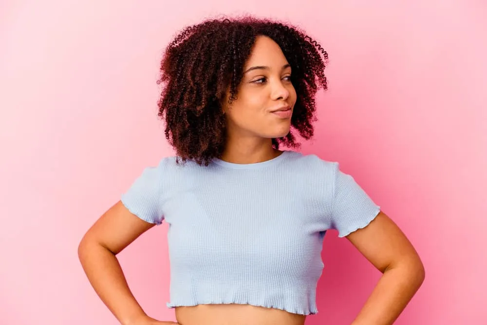 Young black girl wearing a blue t-shirt with tight ringlets like most natural hair types with natural black hair strands.