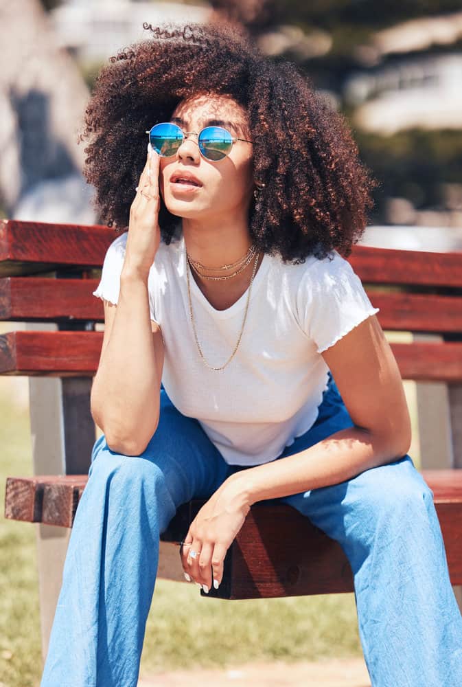 A young stylish woman with curly natural hair is showing her improving hair growth after using coconut oil on her curly hair strands.