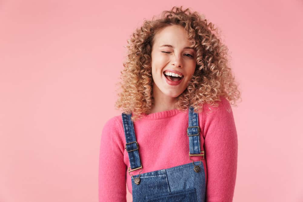 A young girl with curly hair has a dark brown natural hair color, wondering about the balayage cost for highlighting individual strands. 