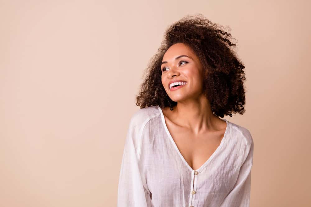 Adorable African American female with curly natural hair has been using essential oils to promote hair growth.