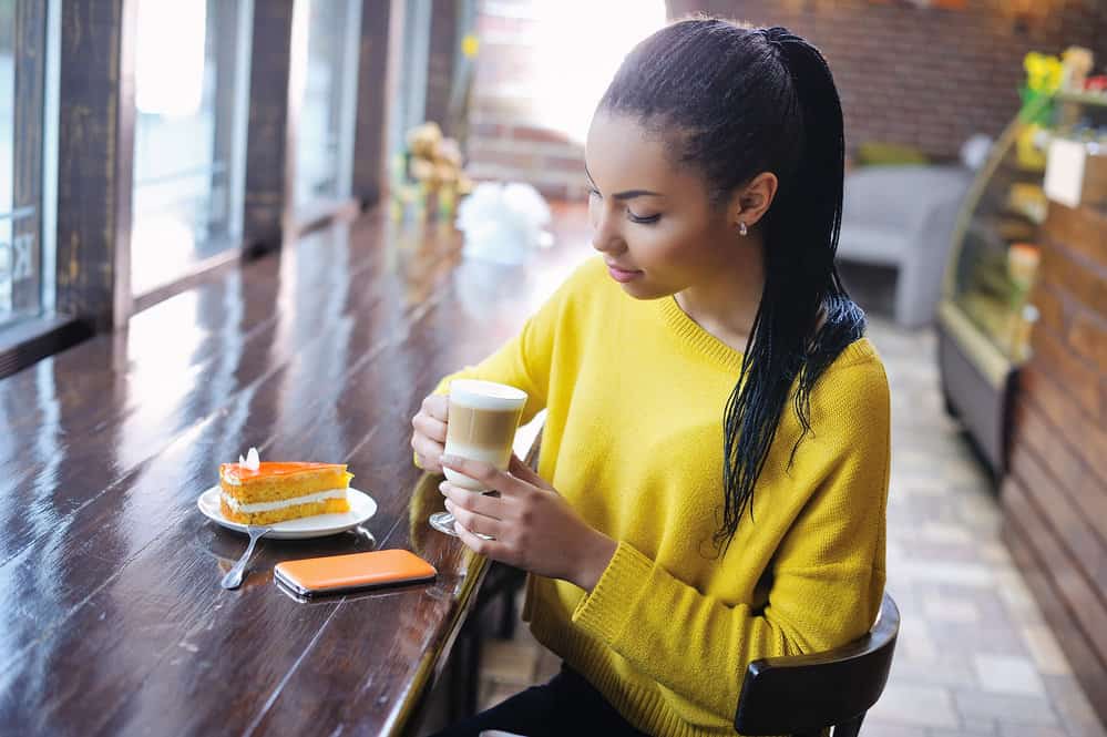African American female wearing micro locks on her 4B healthy hair strands while she drinks a coffee at a local shop.