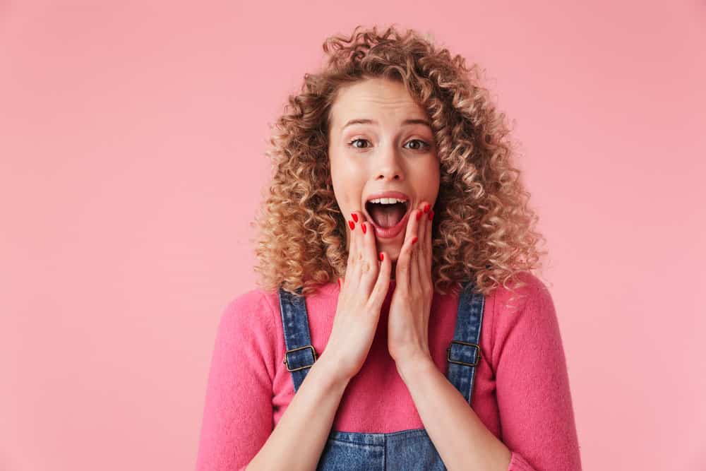 An excited young girl with a 2C hair type and a rock balayage style that involves bleaching the hair to create sharp underneath layers.