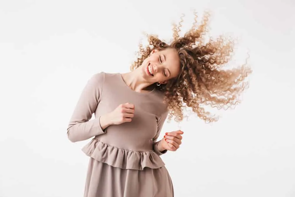 A cute young joyful female with partial highlights is dancing while her longer hair blow in the wind.