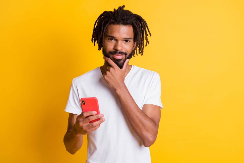 A young black man, after dyeing the tips of his free-form dreads, is using his iPhone 13 outside.