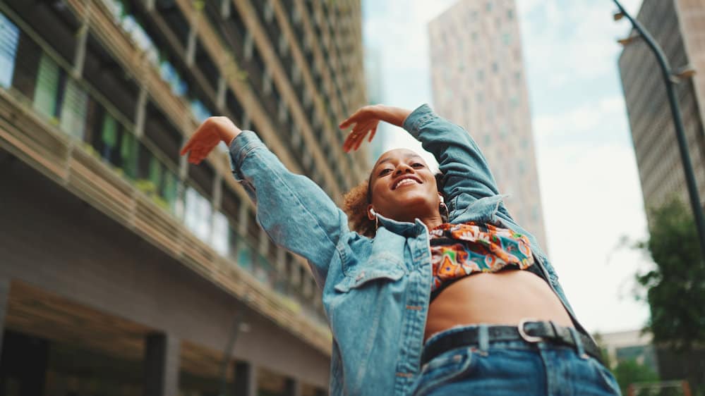 African girl has light brown curls after using a 1:2 bleach ratio while lightening hair is dancing outdoors.