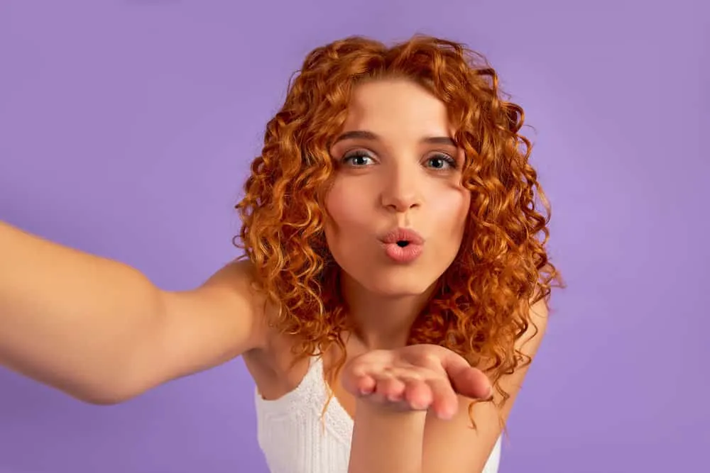 A cute redhead female with a orange hair color after applying purple shampoo to her naturally wavy hair strands.
