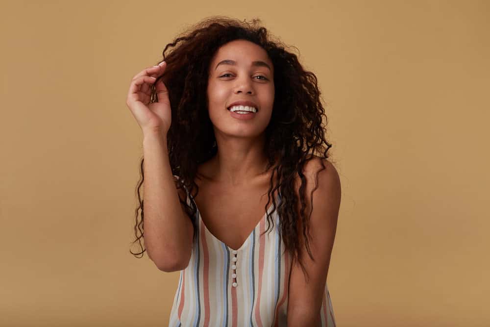 A cheerful brown-eyed female has a full head of waves after removing pin curls and a sock bun with a bobby pin.