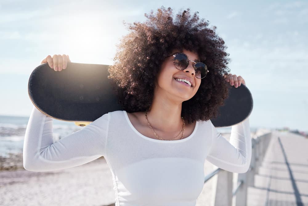 A young African woman with big beautiful curls standing outside on a boardwalk near the beach.