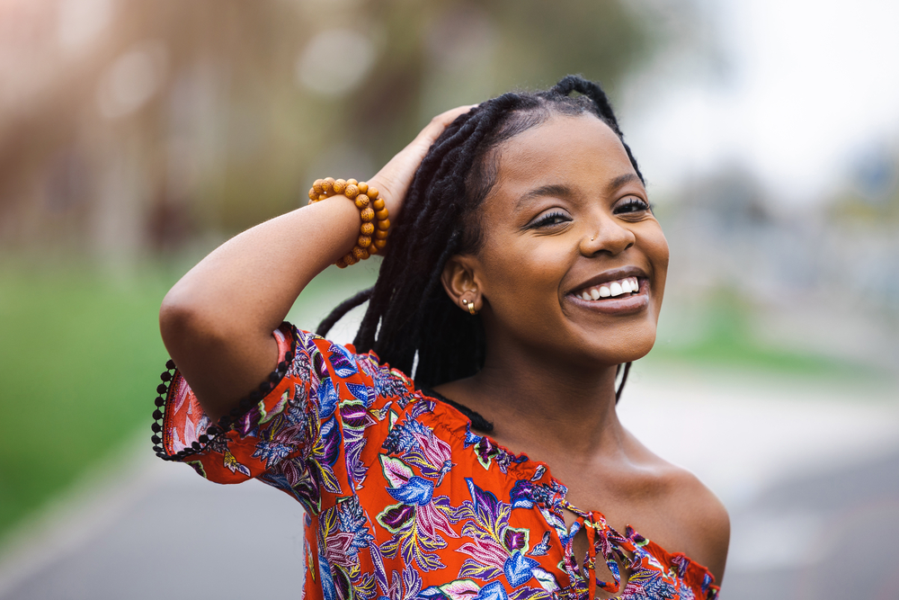 African American lady with a great smile looking at how much hair she has left after using a hair dye removal kit.