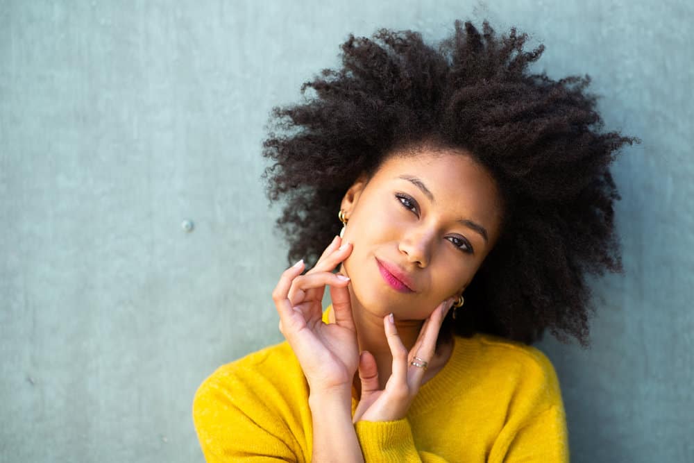 A young lady with a coily curl type has thick, dark brown natural hair strands while wearing a yellow sweater.