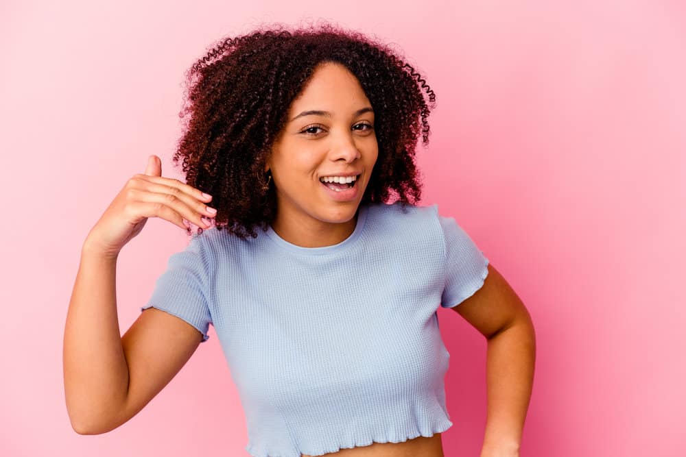 Playful black woman with natural curls styled with a wide-tooth comb, avocado oil, and styling cream.