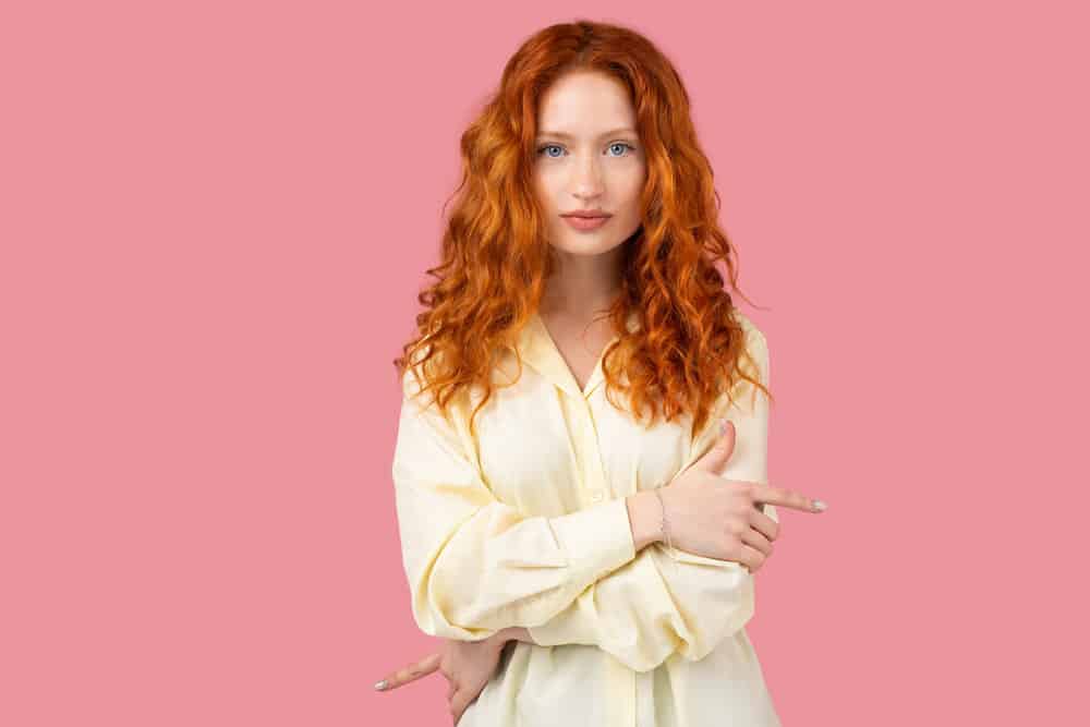 An elegant redhead female with wavy locks that has been treated with the Curly Girl hair care routine.